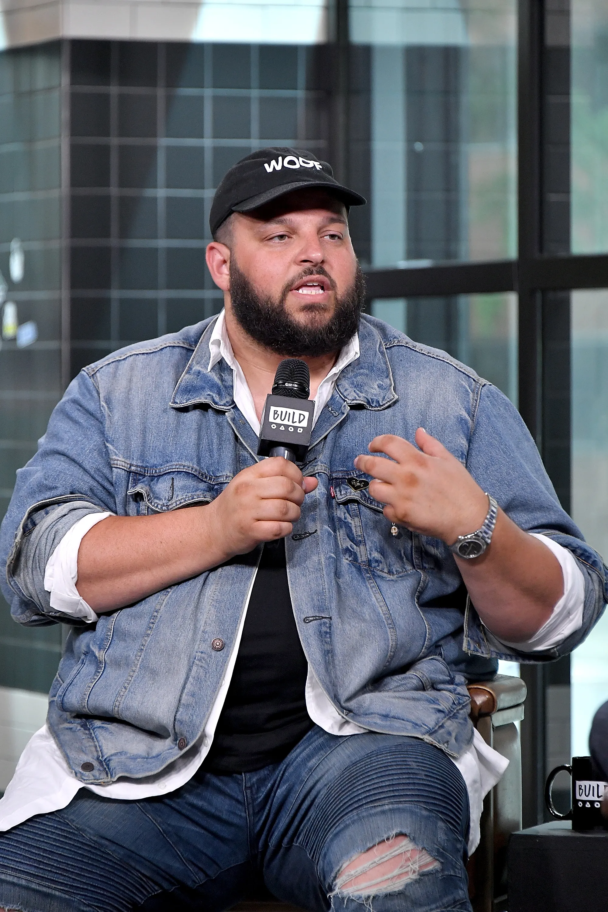 Actor and comedian Daniel Franzese speaks during a visit to Build Studio, holding a microphone and gesturing with his hand.