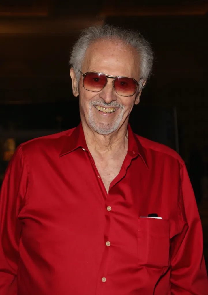 Actor Michael Forest wearing a red shirt and tinted glasses.