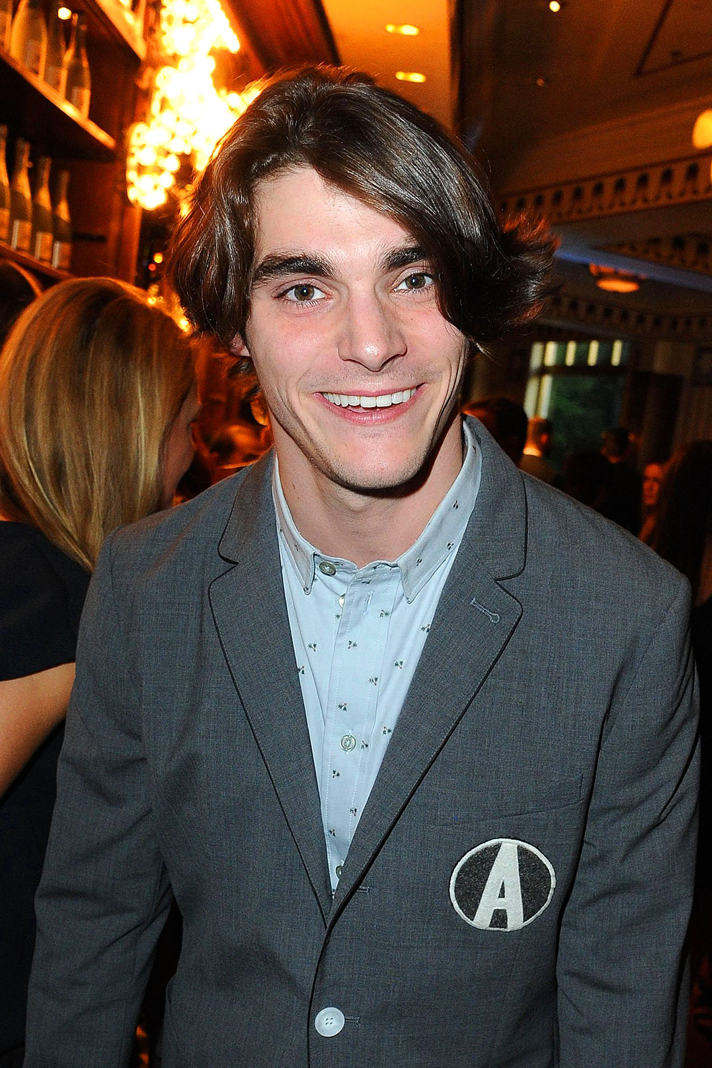 Actor RJ Mitte smiling in a grey blazer.