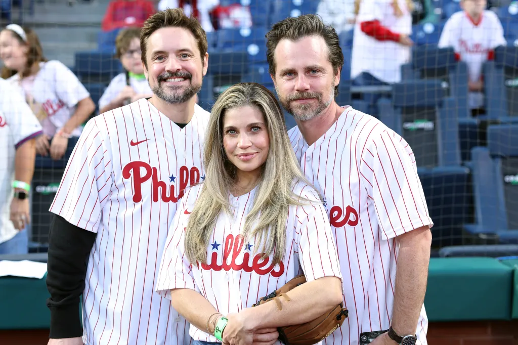 Will Friedle, Danielle Fishel, and Rider Strong pose wearing Philadelphia Phillies jerseys at a baseball game.