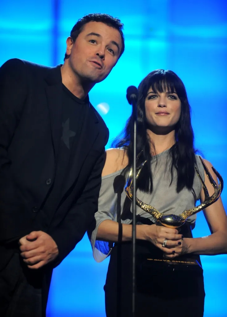Actors Seth MacFarlane and Selma Blair on stage at an awards ceremony, with Selma Blair holding an antler-shaped trophy.