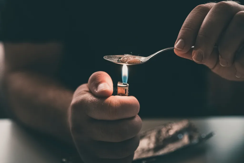 Close-up of a person holding a lighter beneath a spoon containing drugs.