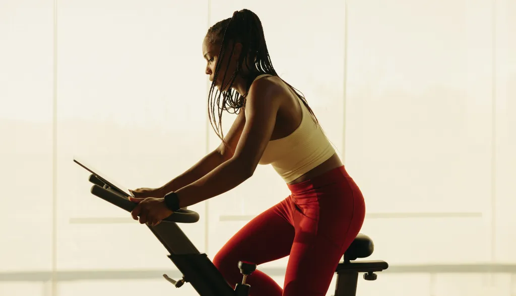 An African American woman is doing cardio on an exercise bike in a gym.