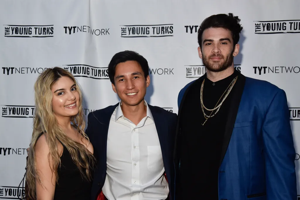 Aida Chavez, Sam Sacks, and Hasan Piker pose in front of a branded backdrop.