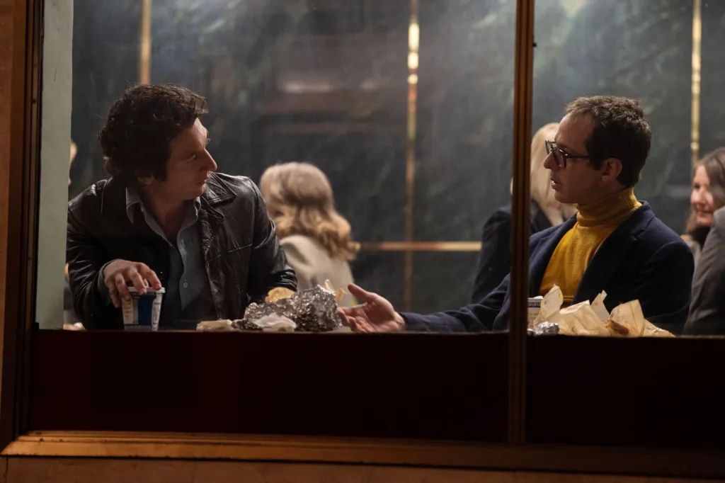 Jeremy Allen White as Bruce Springsteen and Jeremy Strong as Jon Landau sitting in a restaurant booth, seen through a window.
