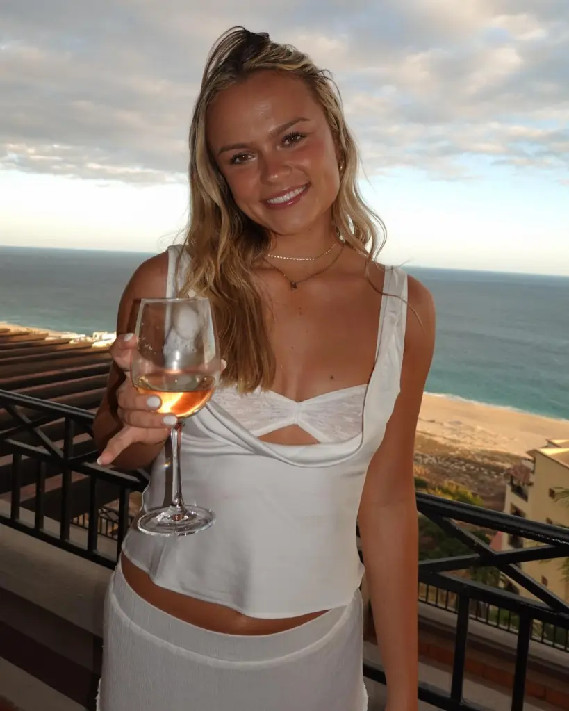 Alana Nielson holding a glass of wine on a balcony overlooking the ocean.