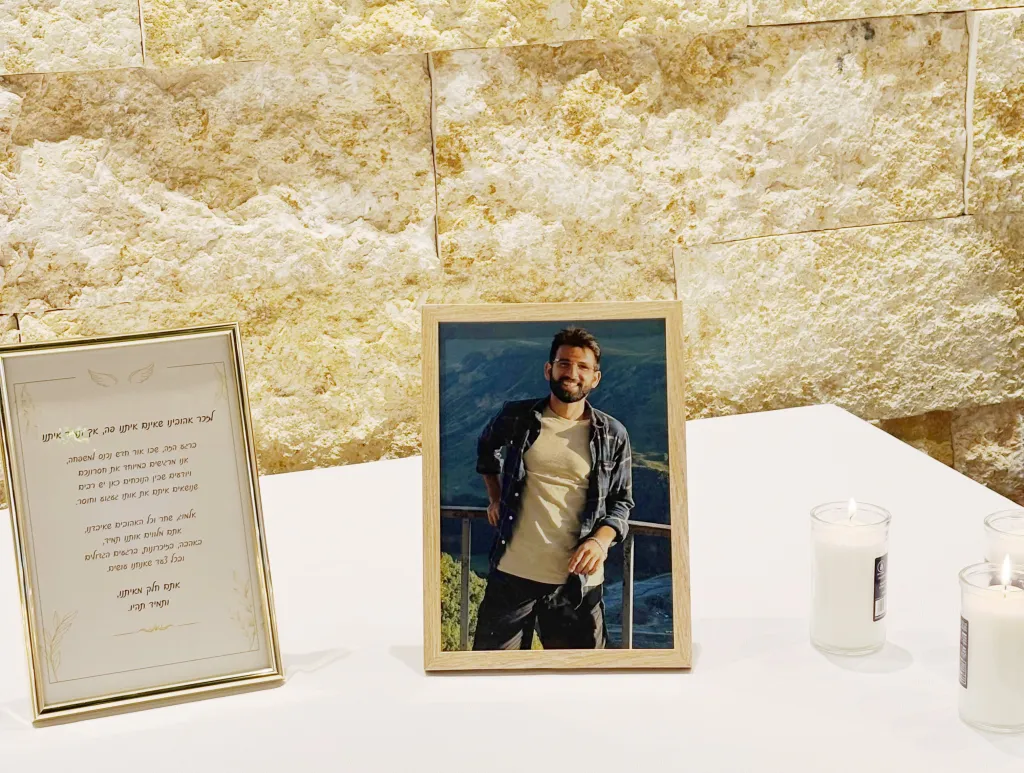 Almog Sarusi, killed at age 27, in a framed photo on a table with memorial candles and a framed message.