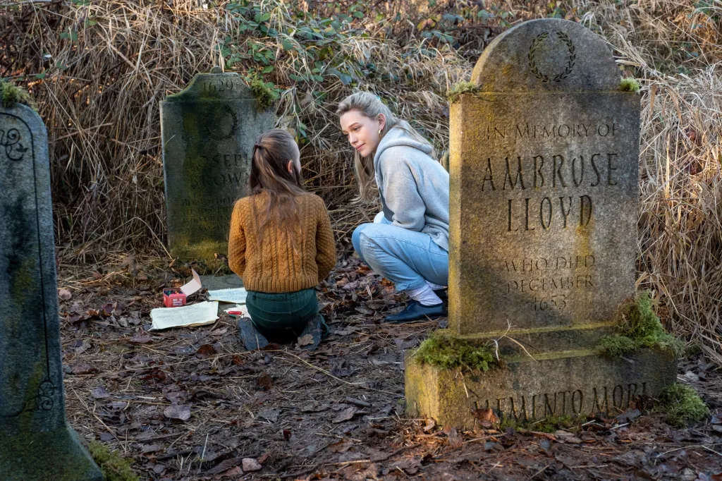 Amelie Bea Smith and Victoria Pedretti crouch among tombstones in a graveyard.