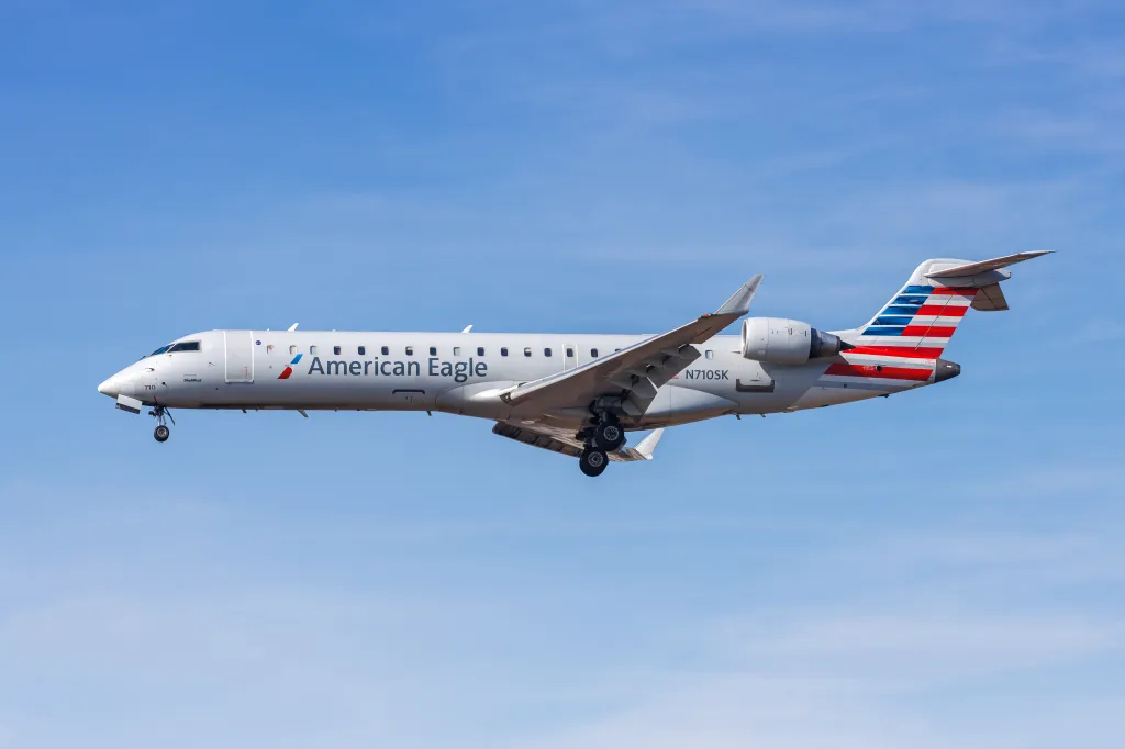 American Eagle SkyWest Airlines Bombardier CRJ700 airplane in flight against a blue sky.