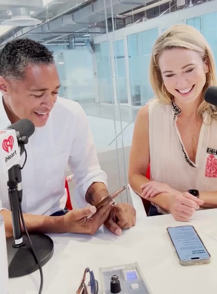 Amy Robach and T.J. Holmes smiling while looking at a phone in a recording studio.