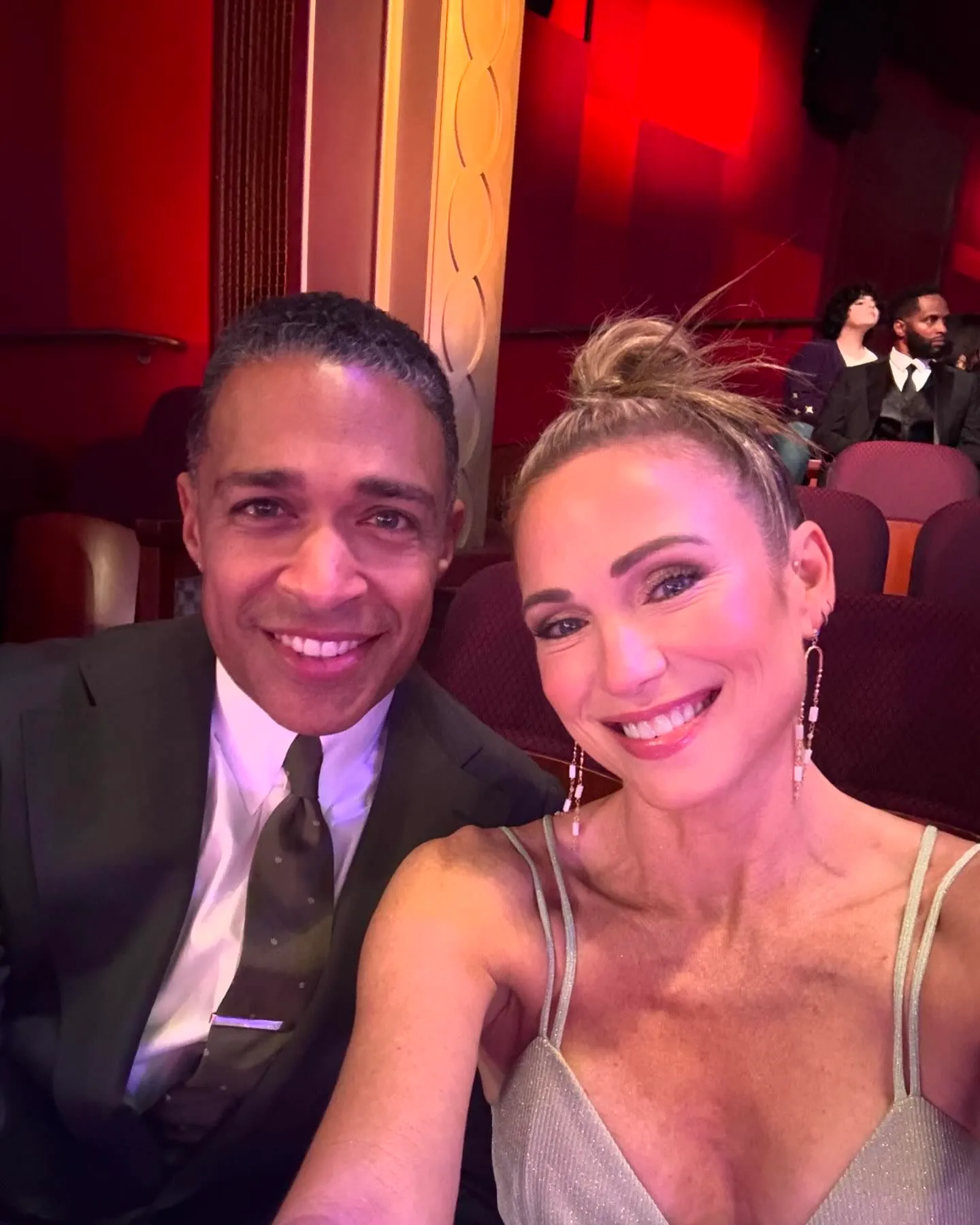 Amy Robach and TJ Holmes posing for a selfie in an auditorium.