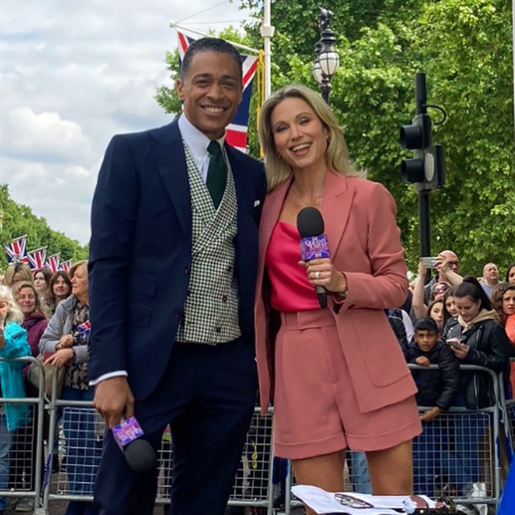 TJ Holmes and Amy Robach standing outdoors holding microphones with a crowd in the background.