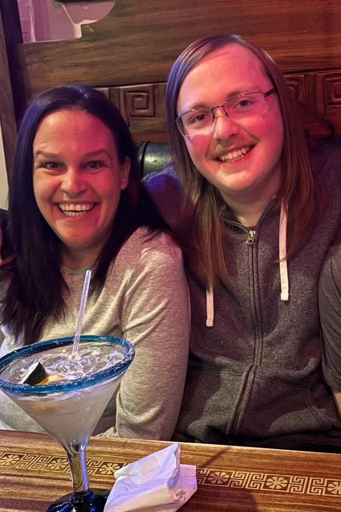 Andria Hanafin smiling alongside her son, Ryan Hanafin, in a restaurant with a drink on the table.