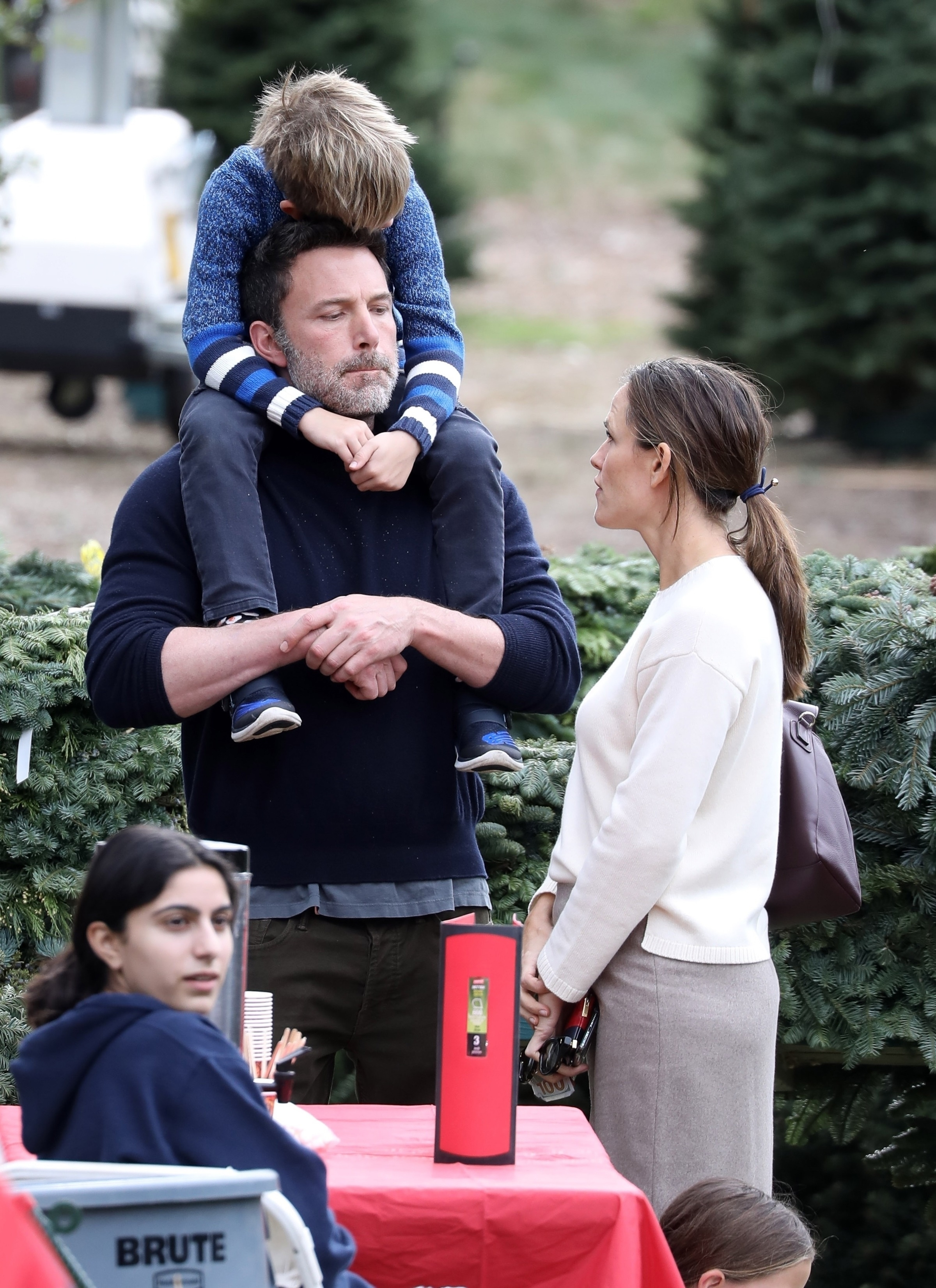 Ben Affleck and Jennifer Garner standing near Christmas trees, with Affleck holding a child on his shoulders and Garner looking toward him.
