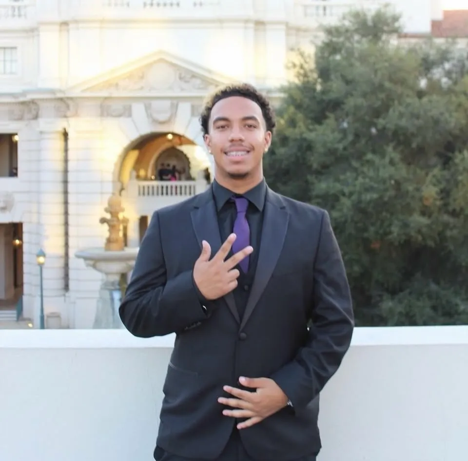 Anthony Joseph Blas in a suit with a purple tie, posing in front of a building.