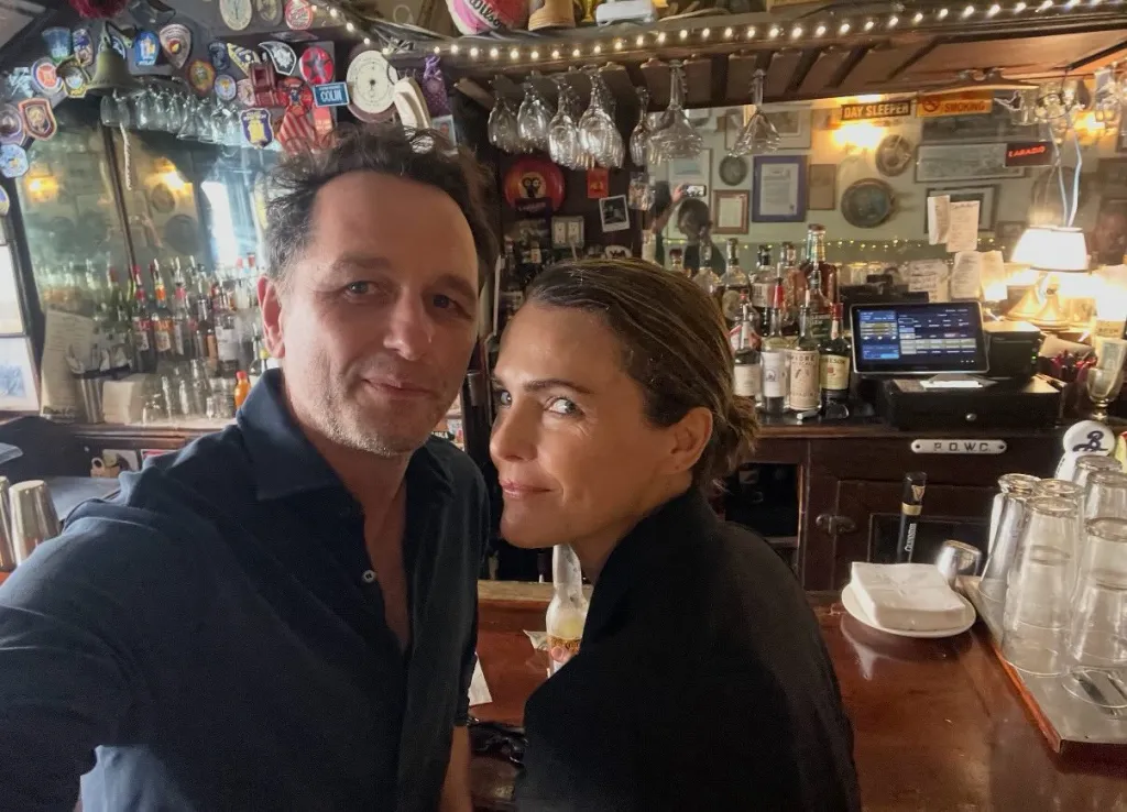 Matthew Rhys and Keri Russell pose together inside a cozy bar.