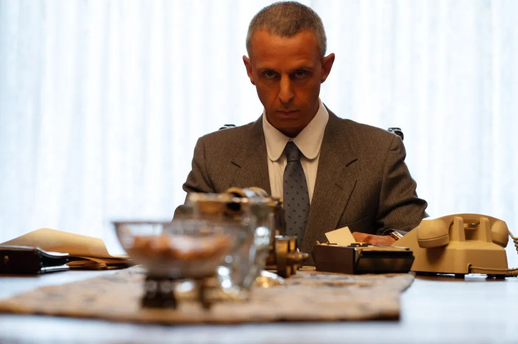 Jeremy Strong as Roy Cohn seated at a desk in a suit and tie in the film 