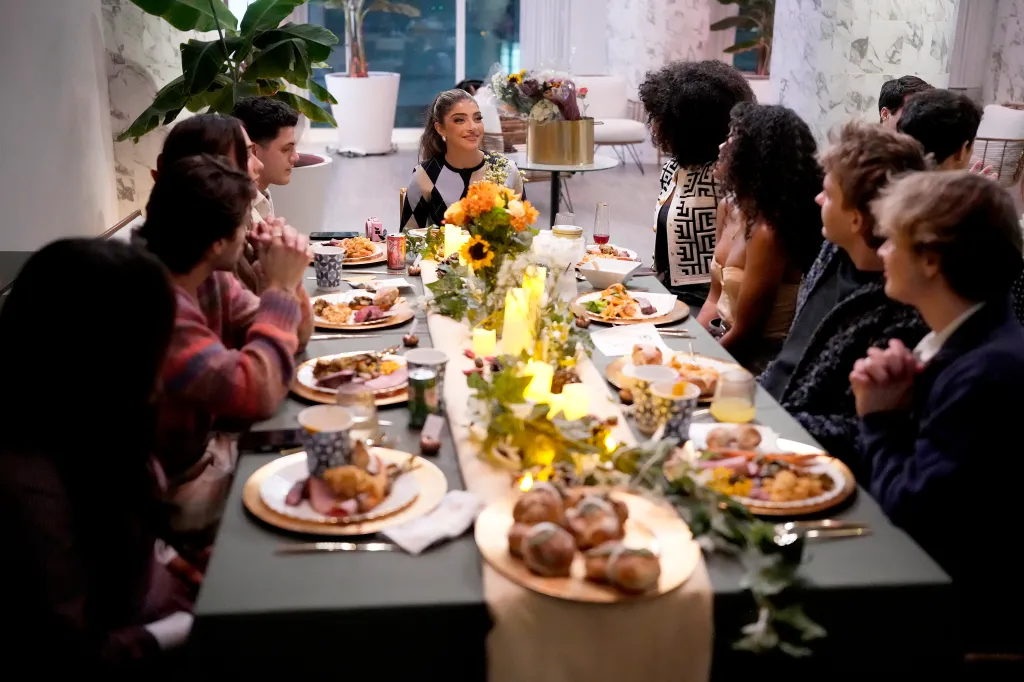 A group of people seated around a long dining table decorated with candles and floral centerpieces for a meal.