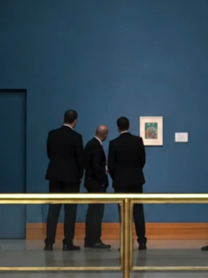 Security personnel view a piece of art hung on a museum wall.