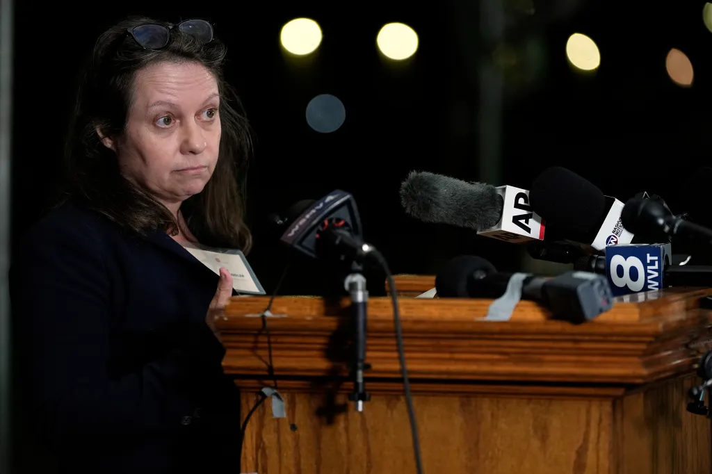 Associated Press reporter Kimberly Chandler speaks at a podium in front of multiple microphones.