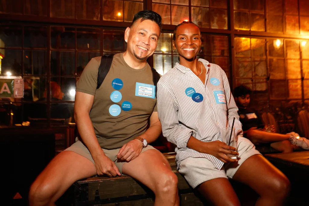 Two people wearing name tags and descriptive stickers sit together at the Sassafras Saloon roommate mixer in Los Angeles.