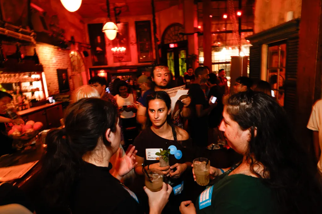 People mingling and holding drinks at a crowded Speed Roommating event inside a dimly lit bar.