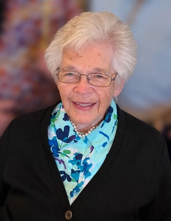 Portrait of Donna Jean Puckett smiling with short white hair, glasses, a blue floral shirt, and a black cardigan.