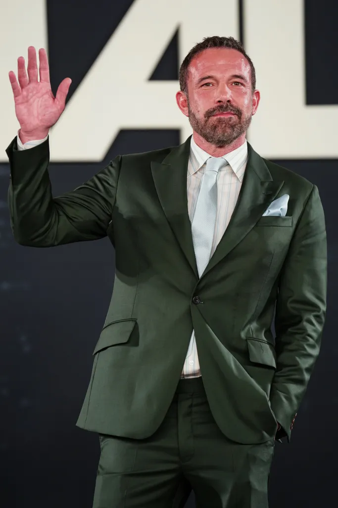 Ben Affleck in a dark green suit waving at the 