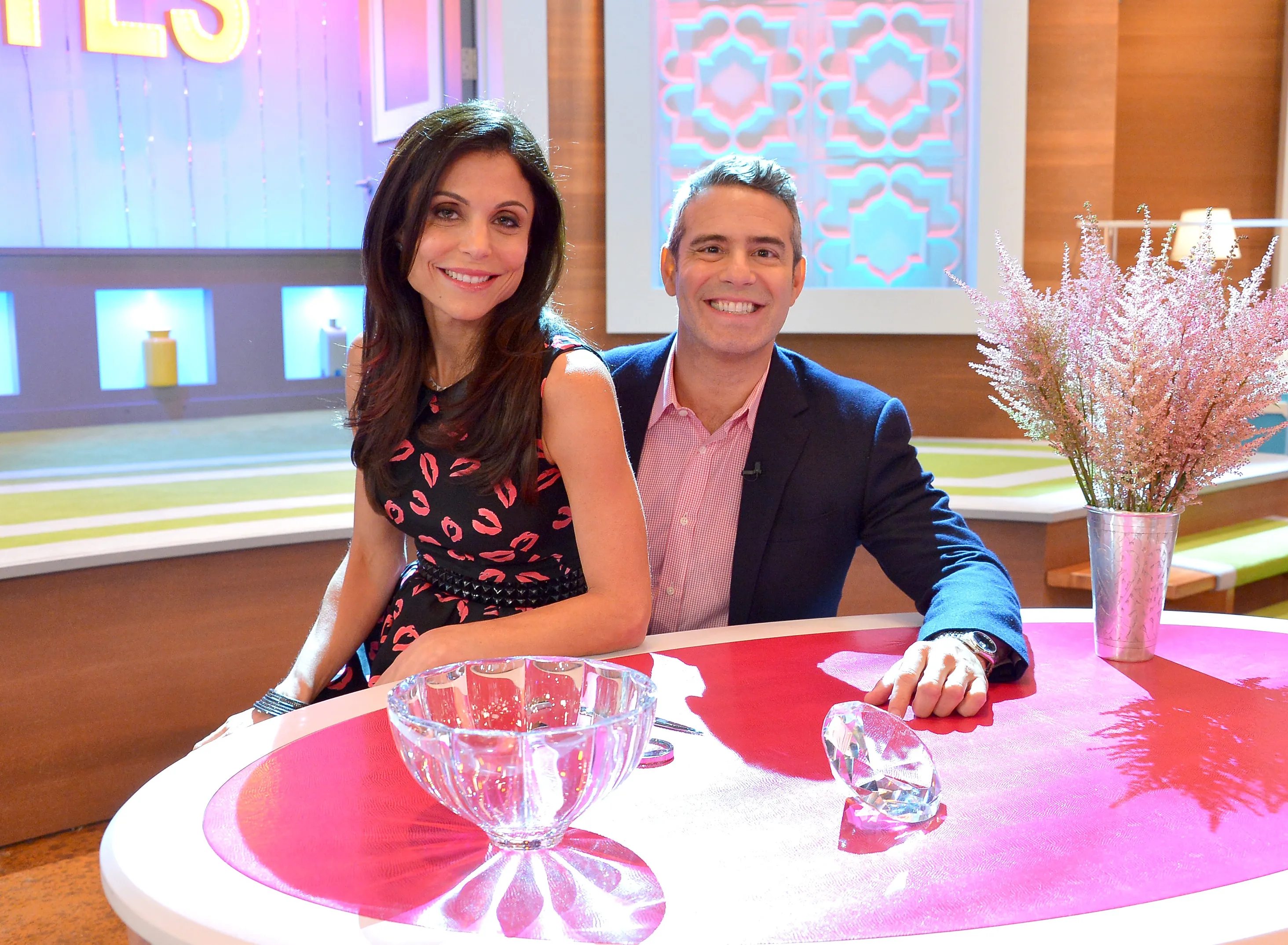 Bethenny Frankel and Andy Cohen smiling together in a studio setting.