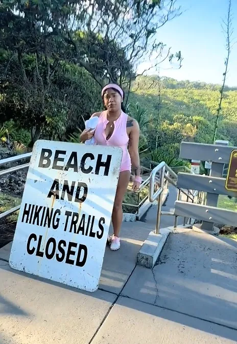A person in pink athletic wear stands behind a sign that reads 