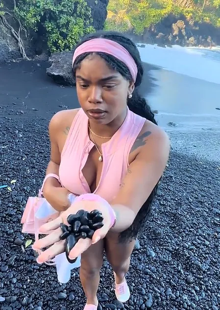 A person holds black volcanic stones in their hand on a black sand beach in Maui, Hawaii.