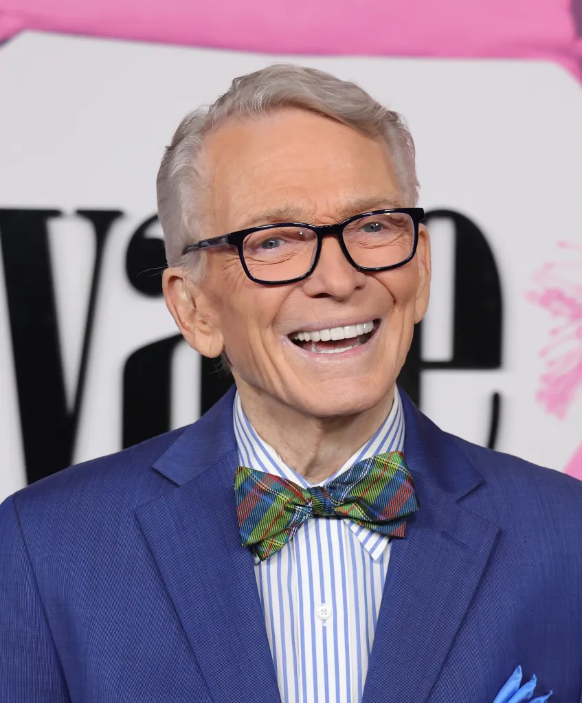 American fashion designer Bob Mackie wearing glasses and a blue suit with a plaid bow tie.