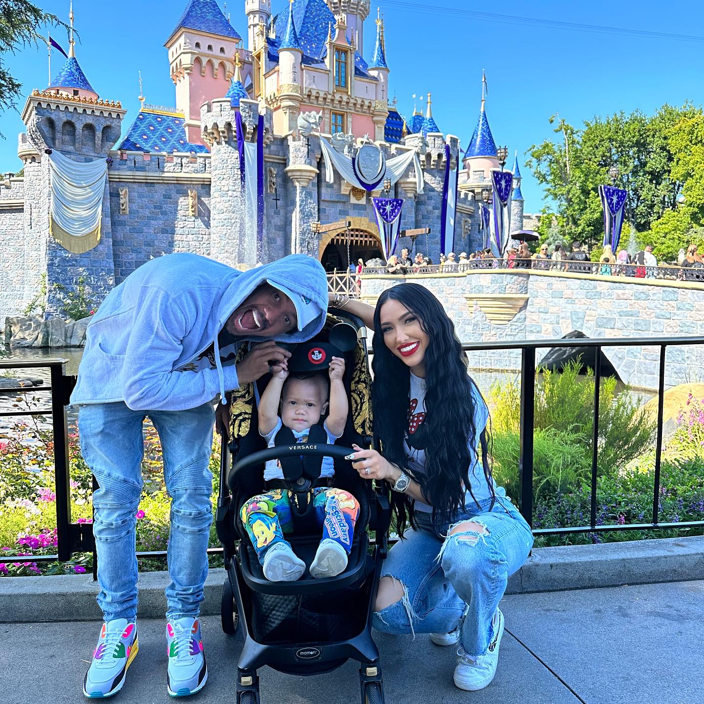 Nick Cannon and Bre Tiesi posing with their baby in a stroller in front of a castle at an amusement park.