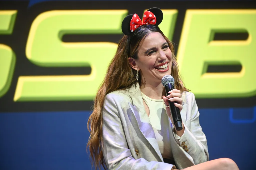 Christy Carlson Romano wearing Minnie Mouse ears and speaking into a microphone at the D23 Expo.