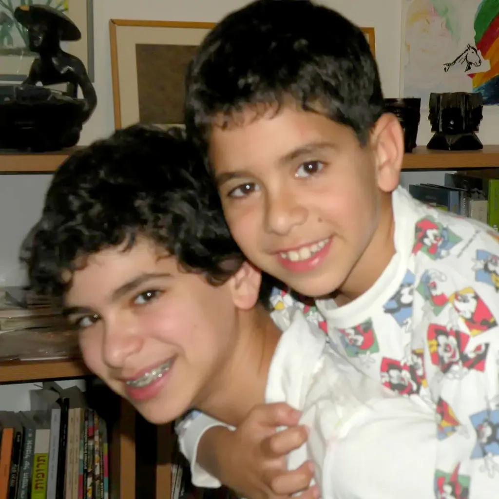 Israeli hostage Evyatar David on the right and his brother Ilay on the left, smiling together indoors.