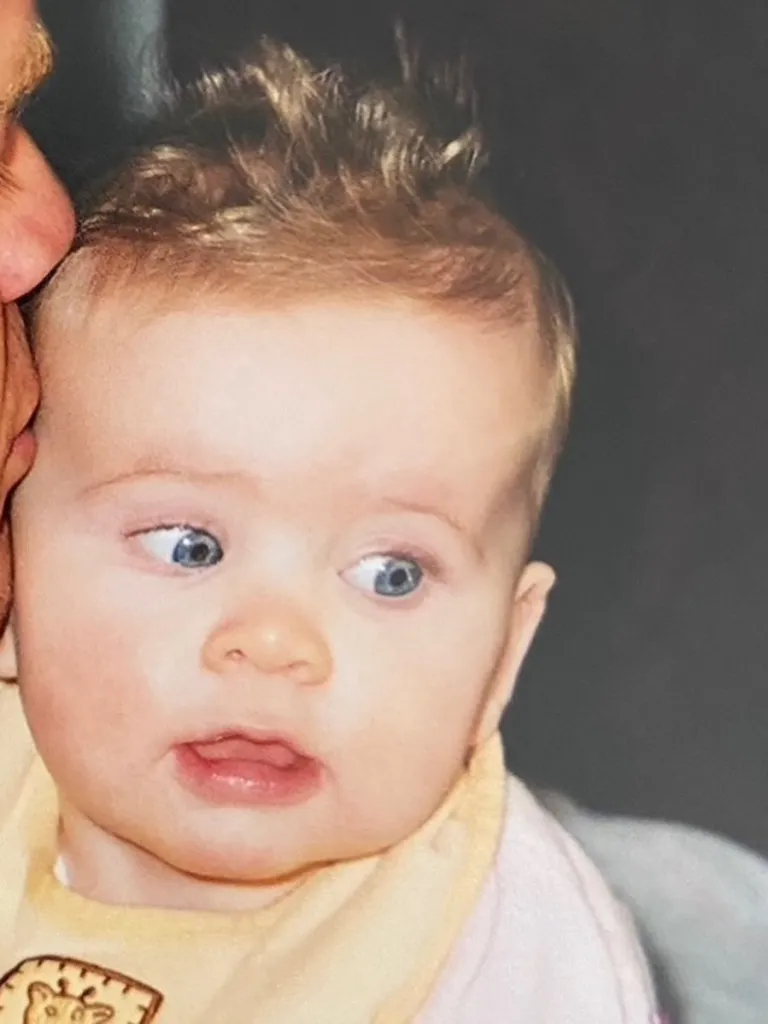 A vintage photograph of a baby with wide blue eyes and spiky blonde hair looking to the side.