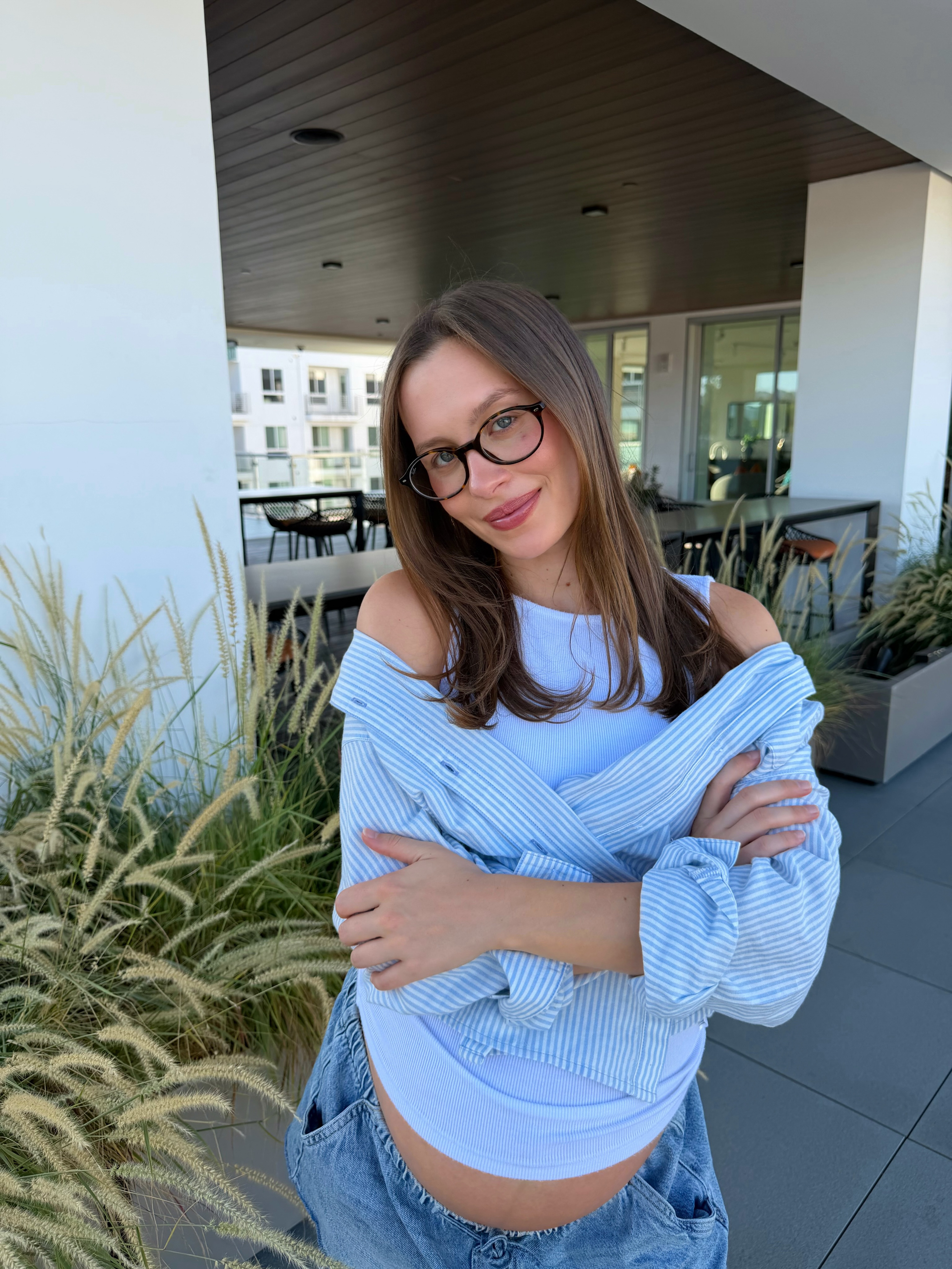 Natasha Bure, Candace Cameron Bure’s daughter, smiling with her arms crossed, revealing her bare pregnant belly.