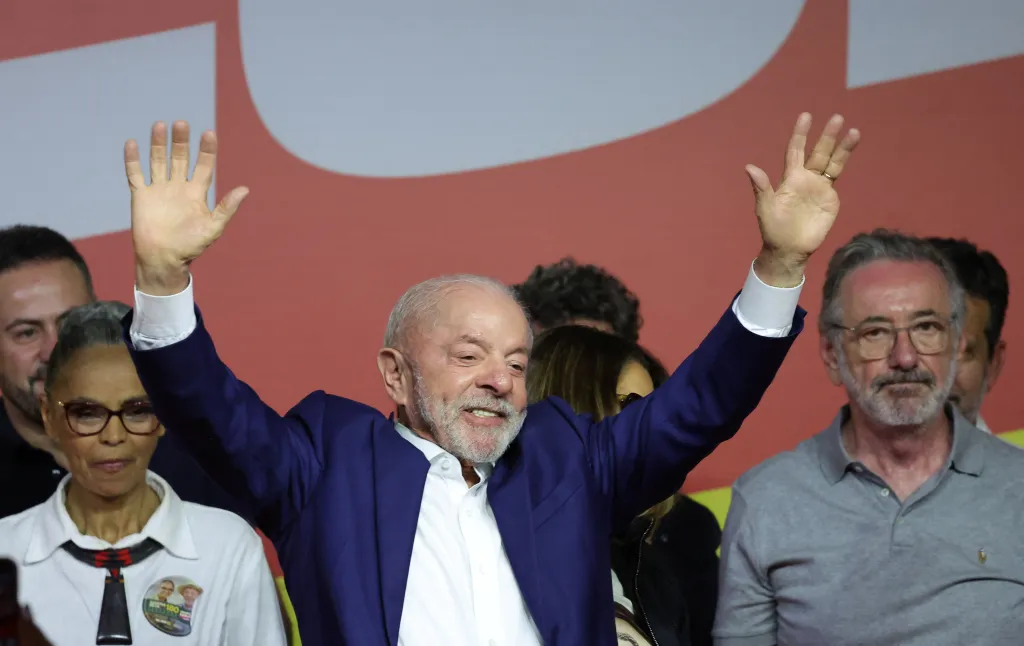 Brazilian President Luiz Inacio Lula da Silva waving with both hands while surrounded by supporters.