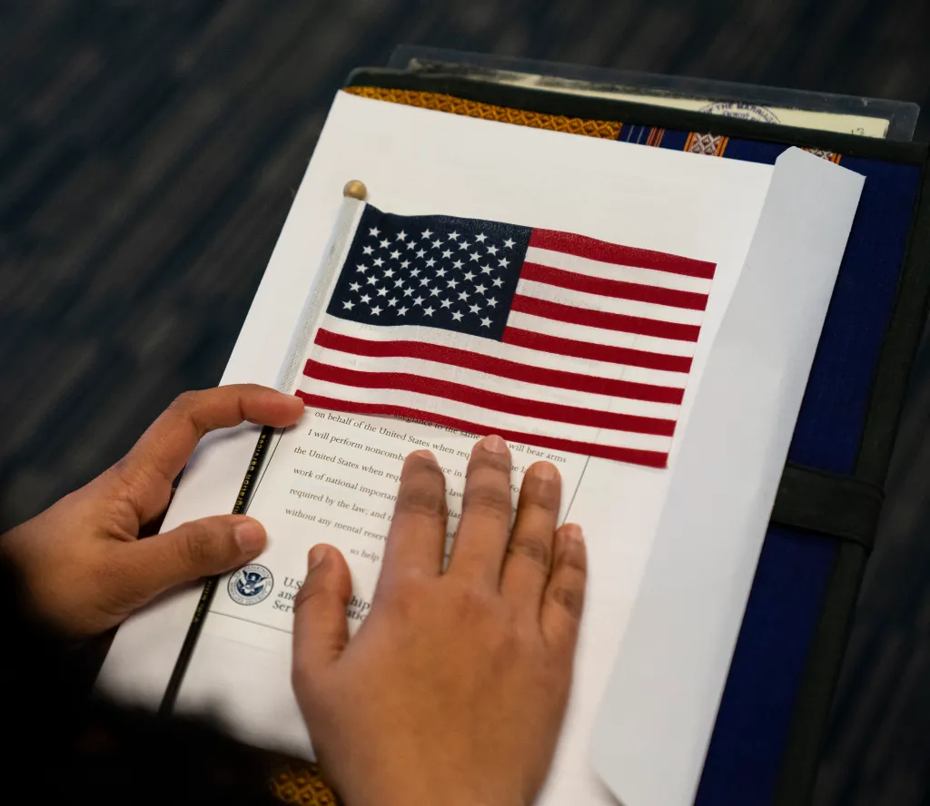 A candidate for U.S. citizenship holds a small American flag over their naturalization paperwork during a ceremony.