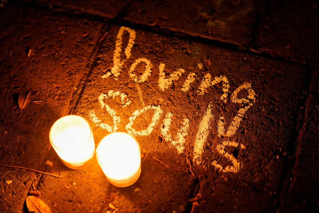 Two lit candles placed next to a message written in chalk on the ground that reads 