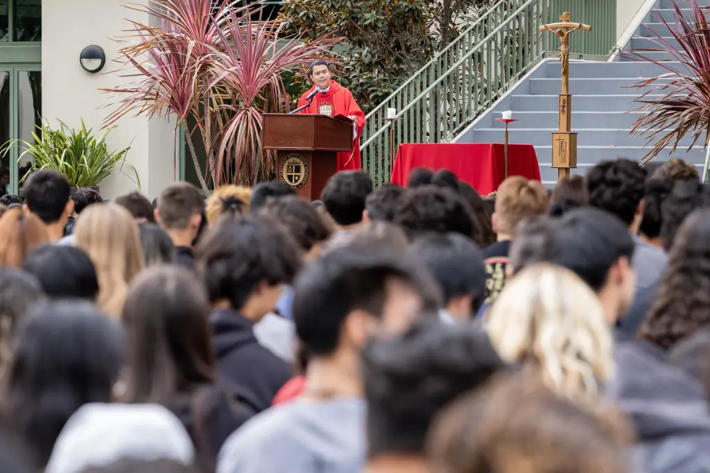 A priest speaks at a podium in front of a crowd of students at Archbishop Mitty High School.