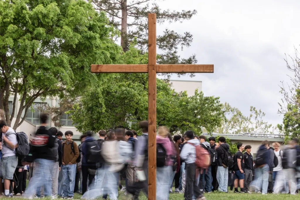 Archbishop Mitty High School campus with a large wooden cross in the foreground and students walking by.