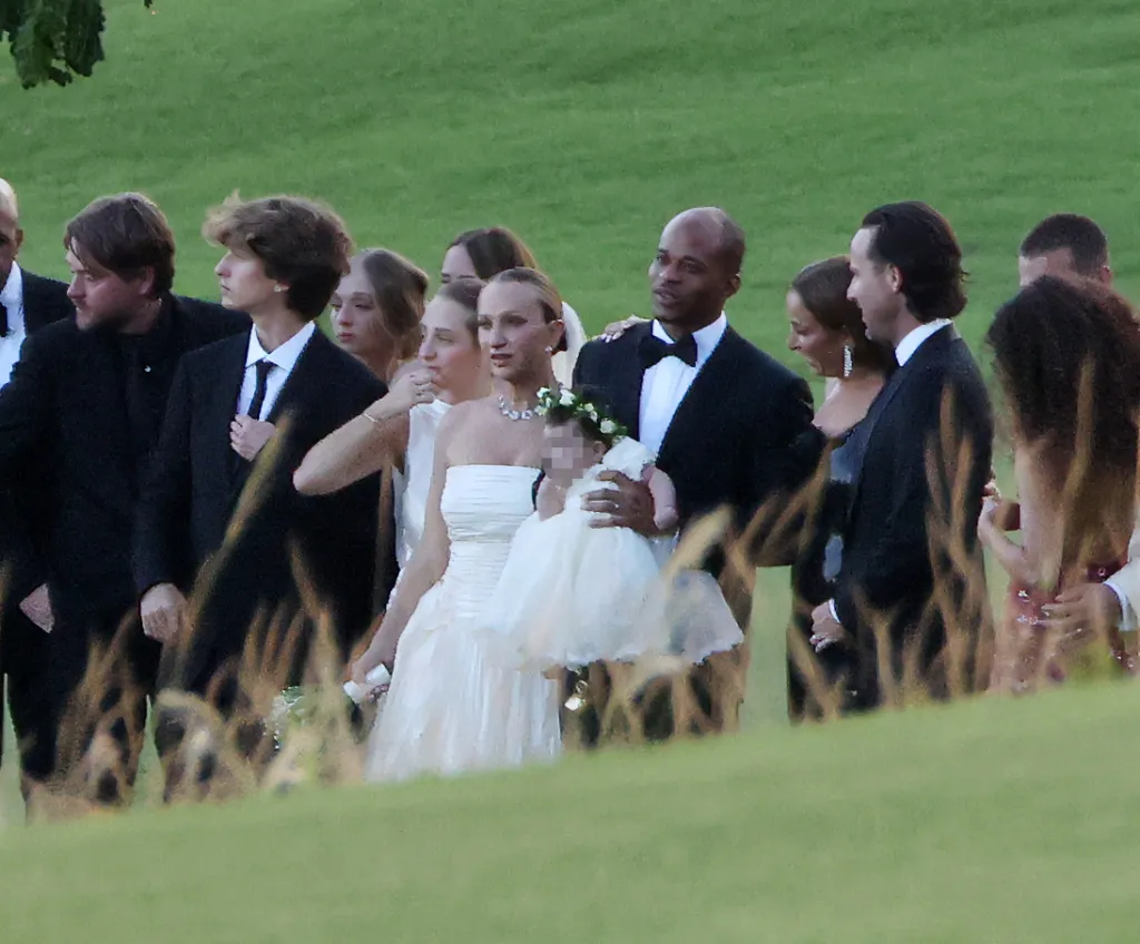 Jennifer Meyer in a wedding dress holding a baby, alongside Geoff Ogunlesi and wedding guests.