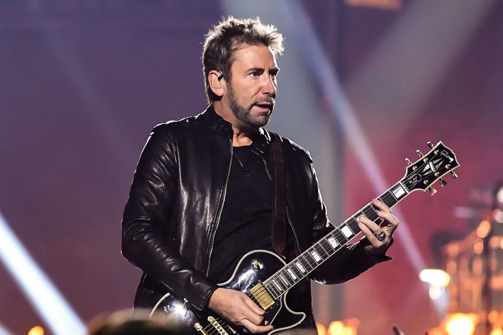 Chad Kroeger playing an electric guitar on stage in a black leather jacket.