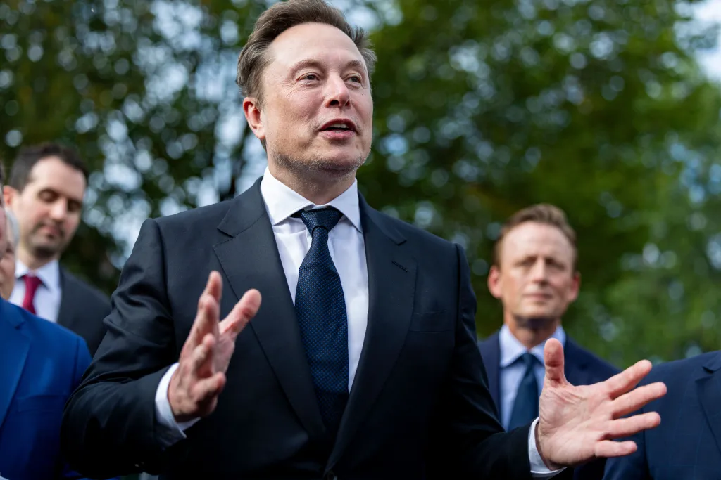 Elon Musk speaks outside the West Wing of the White House, gesturing with his hands.