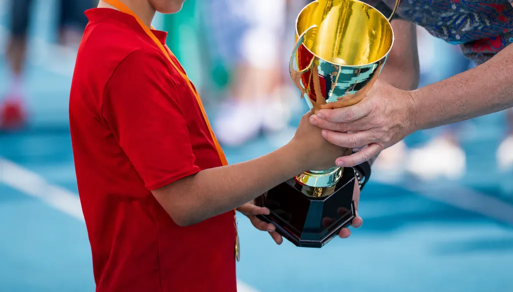 A child in a red sports shirt receives a golden trophy cup.