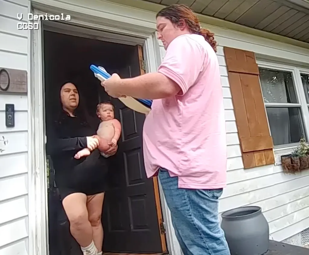 Bodycam footage of Justine May holding one of her children while standing in the doorway talking to an official.