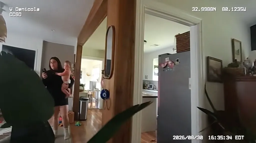 Police body camera footage shows Justine May holding a child indoors.