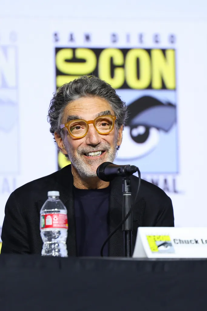 Chuck Lorre at a panel event, seated at a table with a microphone and a water bottle in front of a San Diego Comic-Con backdrop.