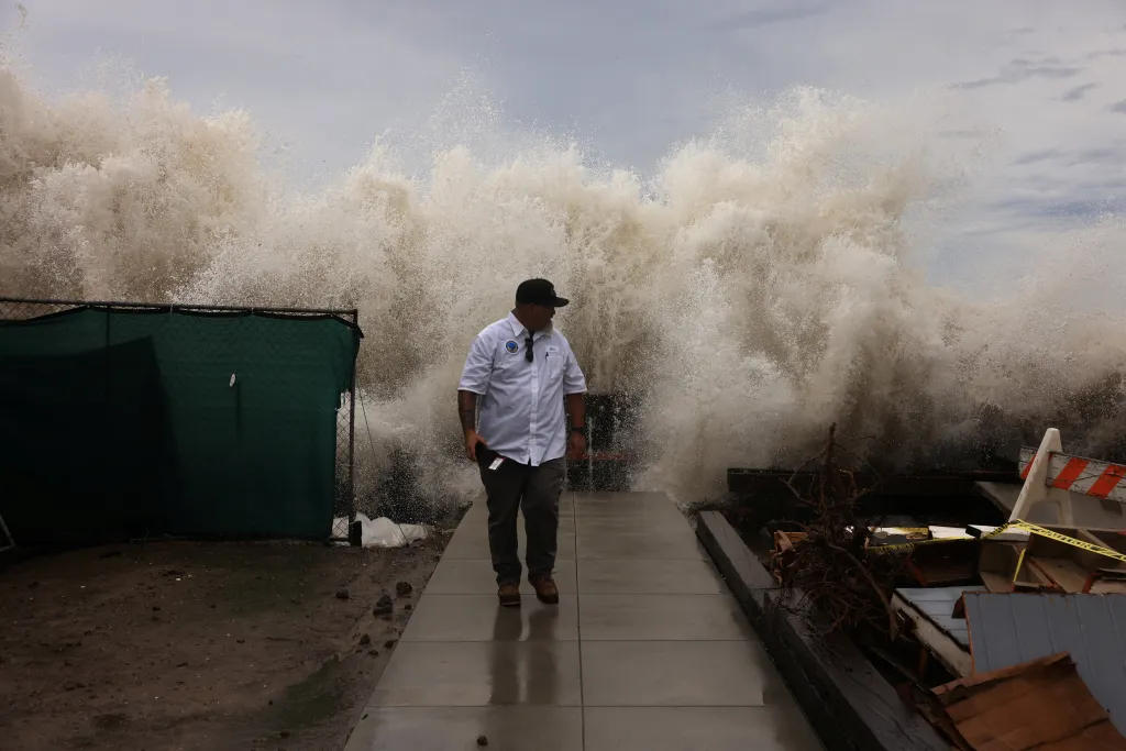 A city worker walks away from a boardwalk as waves generated by Tropical Storm Rachel crash over it in Long Beach, California.